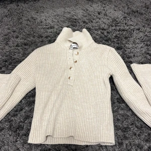Beige ribbad polotröja från BHKA - Säljer en stilren beige ribbad polotröja från BHKA. Tröjan har långa ärmar och knappar framtill som ger en snygg detalj. Perfekt för kyligare dagar.