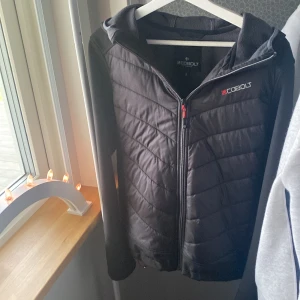 Svart jacka från Cobolt - Säljer en svart jacka från Cobolt med dragkedja och huva. Jackan har en quiltad design på framsidan och är långärmad. Perfekt för kyligare dagar.