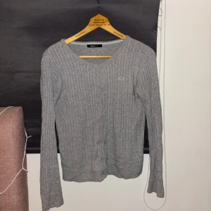 Grå ribbad kofta från Gina Tricot - Säljer en stilren grå kofta från Gina Tricot i storlek S. Den är ribbad och har långa ärmar med knappar framtill. Perfekt för lager-på-lager under kyligare dagar.