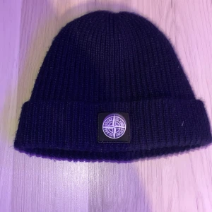 Svart ribbad mössa från Stone Island - Snygg svart ribbad mössa från Stone Island med deras ikoniska logga framtill. Köptes för 1000kr och använts fåtal gånger. Riktigt fet mössa till vintern