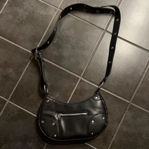 Svart axelväska med nitar - Snygg svart axelväska med justerbar rem och dragkedja. Väskan är sparsamt använd. 