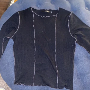 Svart ribbad tröja från Bik Bok - Snygg svart ribbad tröja från Bik Bok med kontrasterande sömmar. Tröjan har långa ärmar och en stilren design som passar perfekt till vardags eller en utekväll. Perfekt för höst och vinter!