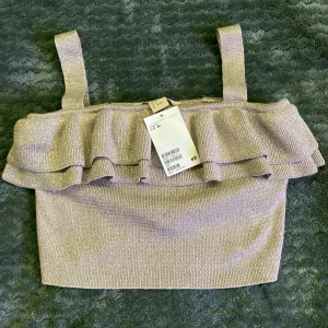 Glittrig guld topp från H&M - Säljer en helt ny oanvänd glittrig topp från H&M med volangdetaljer. Toppen har breda axelband och en croppad passform, perfekt för festliga tillfällen. Den har prislappen kvar! ✨🥂