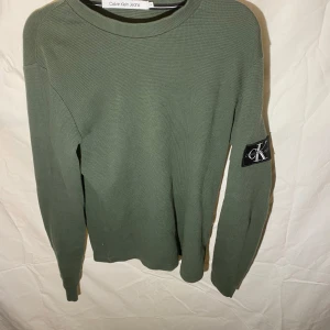 Grön tröja från Calvin Klein Jeans - Snygg grön tröja från Calvin Klein Jeans med långärmad design och ett stilrent märke på ärmen. Inga defekter och sparsamt använd 