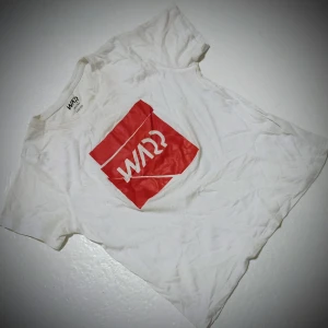 Vit t-shirt med röd logga från Warp - Säljer en vit t-shirt från Warp med en stor röd logga på framsidan. T-shirten har en klassisk passform och korta ärmar, perfekt för en avslappnad stil.