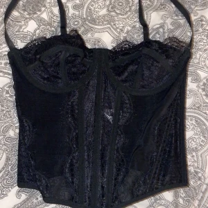 Svart spetskorsett  - Elegant svart korsett med spetsdetaljer och justerbara axelband. Perfekt för en stilfull look med en feminin touch. Snygg till fester!