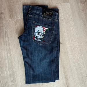 Mörkblå jeans med dödskallebroderi från Ed Hardy - Snygga mörkblå jeans från Ed Hardy med coolt dödskallebroderi på bakfickorna. Jeansen har en straight passform och klassisk femficksdesign. Perfekta för dig som vill ha en unik stil med attityd.