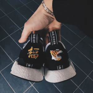 Adidas NMD R1 Neighborhood x Invincible - Unika svarta sneakers från Adidas med broderad tiger och kinesiska tecken på hälen. Skorna har en vit sula och snörning framtill. Perfekta för dig som vill ha en stilren men ändå iögonfallande look.
