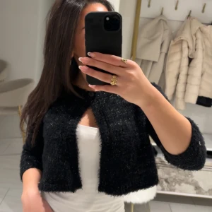 Svart glittrig trekvartsärmad bolerotopp - Snygg svart bolerotopp med glittrig finish. Den är croppad och har trekvartsärmar, perfekt för att lägga till lite glamour till din outfit. Passar bra över en enkel topp för en stilren look. 