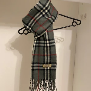 Burberry - Säljer nu denna Snygga halsduk från Burberry i färgen grå. Tillverkad i mjukt lammull med klassiskt fransad kant. Perfekt för att hålla dig varm och stilren under kyliga dagar. Hör av er vid funderingar☺️