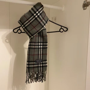 Burberry - Säljer nu denna Snygga halsduk från Burberry i färgen grå. Tillverkad i mjukt lammull med klassiskt fransad kant. Perfekt för att hålla dig varm och stilren under kyliga dagar. Hör av er vid funderingar☺️