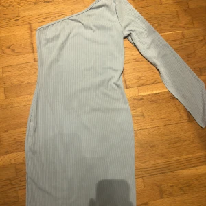 Ljusblå oneshoulder klänning - Snygg ljusblå oneshoulder klänning med ribbad textur. Perfekt för en stilren look med en unik ärm. Klänningen har en tight passform som framhäver figuren.