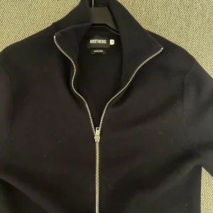 Svart tröja med dragkedja från Brothers - Snygg svart tröja från Brothers med dragkedja framtill. Perfekt för en stilren look. Tröjan har långa ärmar och en hög krage som ger extra värme.