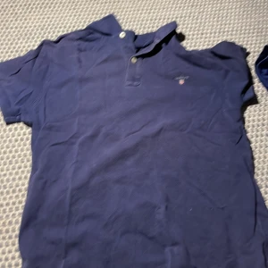 Blå pikétröja från GANT - Snygg blå pikétröja från GANT med klassisk krage och knappar. Perfekt för en avslappnad men stilren look. Broderad logga på bröstet ger en extra touch av elegans.