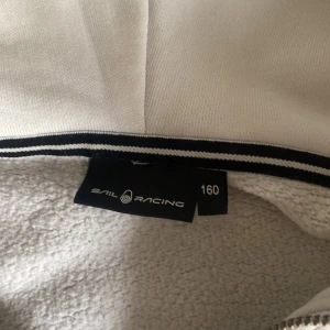 Vit sail racing zip hoodie i storlek 160  - Vit sail racing zip hoodie i storlek 160  köpt från kidsbransstore för 999 kronor, säljer den för 500.  Har haft tröjan i över ett år nu och har haft  den mindre en ett halv år ungefär. Kontakte mig om du är sugen på den