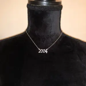 Silverfärgat ”2004” halsband. Läng ca 47cm. Vikt ca 4g.