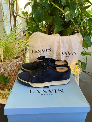 Lanvin Cap Toe Blue Suede Sneaker  - Hej, säljer ett par snygga Lanvin Cap Toe Sneakers i marinblå mocka. Svarta snören i satin som ger en snygg kontrast till mockan. Nypris 4600. Dustbag medkommer. Använda men i bra skick, inga defekter. Size 10= 44/45. Pris kan diskuteras. Hör av dig!