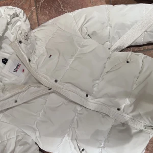 Tommy Hilfiger dunjacka - Vit dunjacka från Tommy Hilfiger. Nypris ca 2000kr. Använd 1 säsong, lite smink på kragen men ej testat tvätta den samt en liten fläck på underarmen
