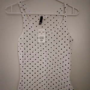 Ny & oanvänd. Vitt linne med svarta prickar. Bomull. Tags sitter kvar. Strlk: XS-SMALL. - Ny & oanvänd. Vitt tunnt linne med svarta prickar. Bomull. Tags sitter kvar. Strlk: XS-SMALL. Felfri.