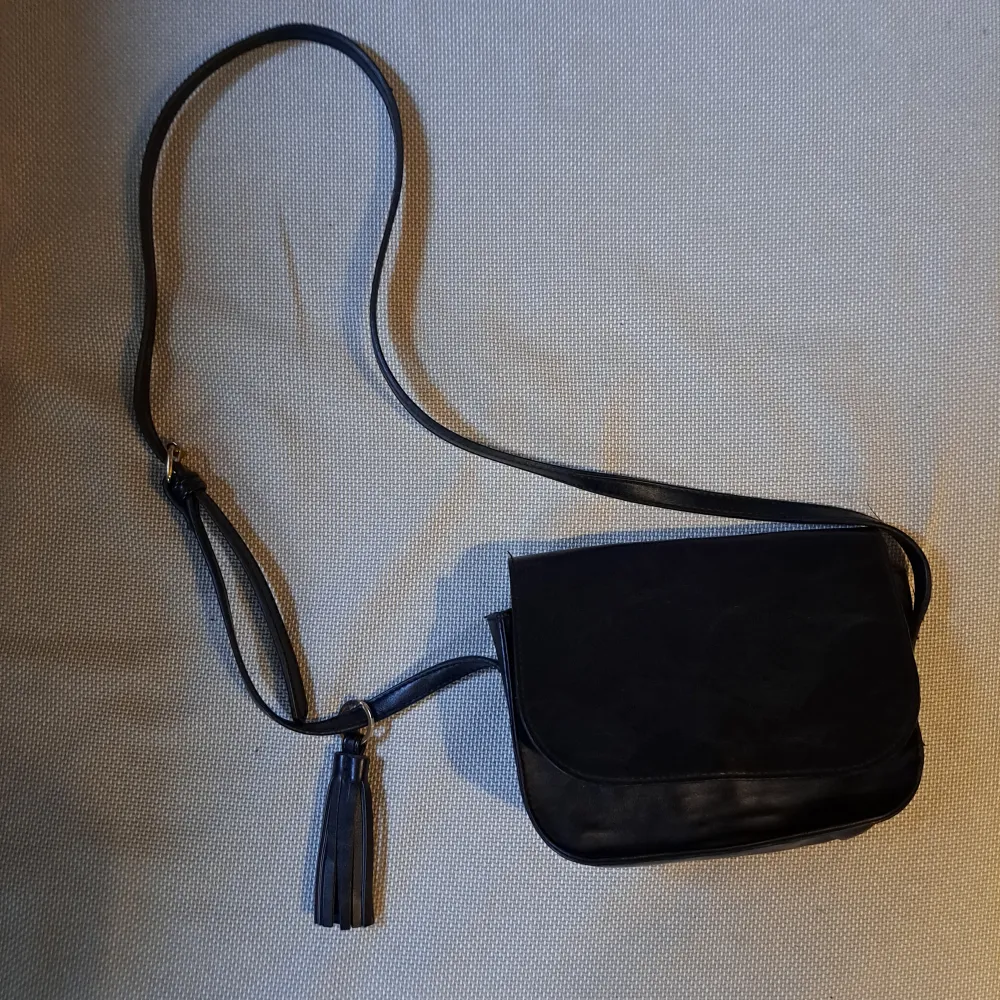 En svart axelremsväska från Even&odd. Väskan är överlag i bra skick förutom missfärgningen på den undre knappen. Väskor.
