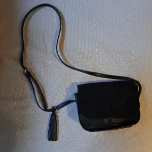 En svart axelremsväska från Even&odd. Väskan är överlag i bra skick förutom missfärgningen på den undre knappen