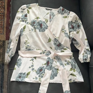 Blommig blus - En fin somrig och blommig blus. Sitter jättefint med en dragkedja på höger sida, kan även knytas med ett tillhörande band rund midjan.