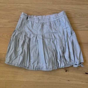 Kjol silvergrå - Plisserad kjol med dragsko längs ned i en silvergrå ljus färg. Dragkedjan på sidan går inte att dra igen sista centimetern men syns ej. 76 cm i midjan och 39 cm lång. 
