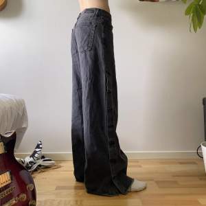 Jättecoola svarta/gråa vida jeans som går att knäppa upp med knappar på sidorna. Stor att storleken är L men passar perfekt low waist på mig som brukar ha s. Midja: 39cm. Skriv om du har fler frågor!