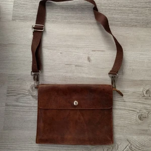 Läderväska  - Brun läderväska i fint skick! Kommer tyvärr inte till användning! Man kan ha både väskan bara över axeln eller tvärs över kroppen! 