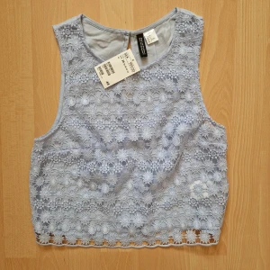 Blommig spetstopp - Jättegullig topp i blommigt spetstyg, babyblå. Aldrig använd, prislappen sitter kvar. Originalpris 199 kr.
