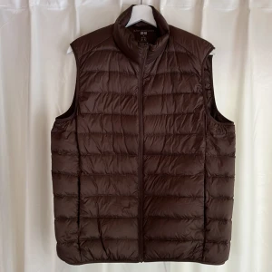 UNIQLO UltraLight dunväst M - Uniqlo dunväst i nyskick. Använd fåtalet gånger, säljes pga fel storlek. Storlek herr M, naturbrun färg. Rak passform, lätt material och dynfylling. Praktisk packpåse och värmande fickor.