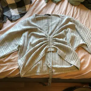 En grå Kroppad tröja med snören i midjan så du kan dra åt tröjan eller släppa ut den som du vill. Tröjan har långa armar och är i lite tjockare kvalitet