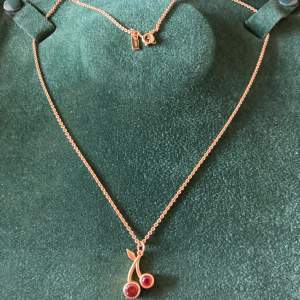 Halsbandet med två röda körsbär från Maria Nilsdotter äkta silver guldpläterat.  Asken ingår inte 