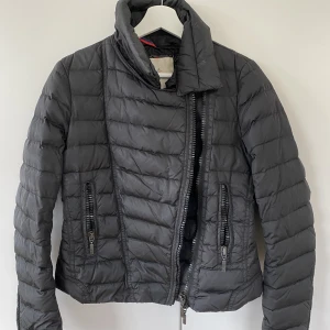 Moncler jacka (biker modell) - Monclerjacka i dun med avtagbar krage. Använd men i gott skick. Serie-etiketten på insidan av jackan är sliten men i övrigt mycket bra skick. Storlek small. 