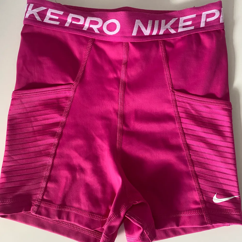 Rosa Nike pro shorts med fickor på sidorna. På baksidan av shortsen finns även en ficka med dragkedja.. Shorts.
