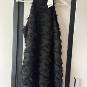 Feather dress - Svart klänning med fjäderliknande stil. Sitter tajtare runt halsen och lösare i övrigt. Oanvänd från BikBok med prislappen kvar. Nypris 500kr.