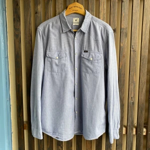 Lee ljusblå skjorta - Ljusblå Lee skjorta med vita detaljer och metallknappar. Några småslitage (kontakta för bilder) siz: M. Pris: 99kr. 