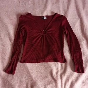 Topp från H&M strl M - En vinröd topp i strl M från H&M med en metallring precis mellan bröstan som piffar upp den lite. Den passar till vardags eller på fest