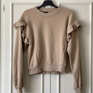 Beige sweatshirt  - Gullig sweatshirt med volanger vid axlarna. Ganska tunt sweatshirttyg, 65% bomull 35% polyester. Begagnat men fint skick! 🌼