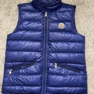 Moncler väst  - Säljer nu min snygga Moncler gui väst! Mycket fint skick och är helt äkta, Qr-kod finns✅. Västen är storlek 12 i junior, sitter som xs. 