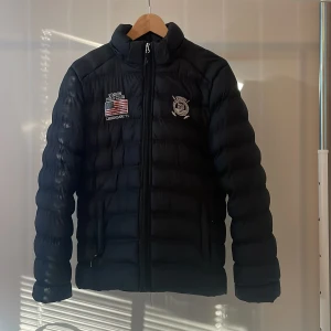 Polo jacka  - En svart polo dunjacka. Jackan är i storlek 16, skulle säga att den passar small. Den är i toppen skick förutom att dragkedjan sitter lite dåligt längst ner men går fortfarande att stänga. Hör av dig för fler bilder eller frågor.