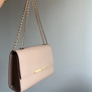 Handväska - Fläckfri elegant väska som går att göra kortare, längre eller mellan längd väldigt simpelt. Lagom storlek. Får plats med allt viktigt i din vardag som ex mobil, korthållare, nycklar, mobil laddare etc (beige/ljusrosa)