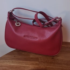 Longchamp axelremsväska - Röd longchamp axelväska i nyskick. Axelremmen går att justera.