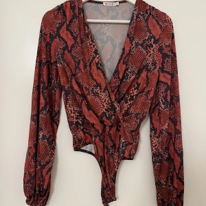 Röd body  - En röd body i ormmönster. Aldrig använd. Köpt på Nelly för några år sedan. 