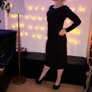 Elegant svart festklänning från Ilse Jacobsen. Den perfekta lilla svarta för alla tillfällen. Läcker v-ringning bak. Dekorativ volang på vänster sida. Midi/knälång. Stretchig & bekväm. Längd 92 cm, byst 80, midja 70, höft 94. Så fin till helgernas fester.