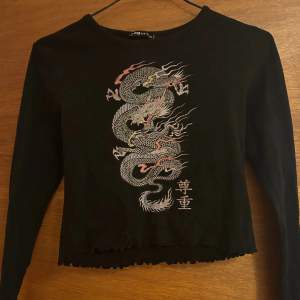 En fin croppad svart tröja med en drake på.