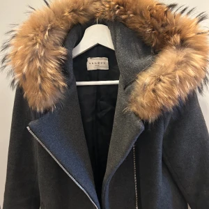 Varm kappa Sandro - Köpte denna kappa för några år sedan, knappt använt den, mest hängt i min garderob. Storlek 36 men är lite liten i storleken. Jag är 167 och den passar min längd men nog inte om man är längre. Inköpt för 3-5 tusen, minns ej exakt. 80% ull och äkta päls.