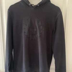 Belstaff hoodie - Belstaff hoodie med svart tryck på bröstet. Den är i använt skick men är skön och fin!  Skriv vid frågor eller funderingar :)