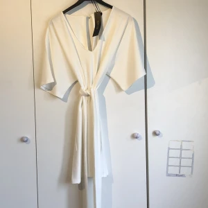 Vit klänning - Vit klänning med knytning i storlek 38/M. Aldrig använd. Tjockt och lyxigt material.