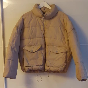 Vinter Pufferjacka Beige NA-KD - Varm och skön pufferjacka/vinterjacka som är sparsamt använd. Den är lite oversized men funkar perfekt på mig som är en S. Finns lite slitage och fläckor (Kan skicka bilder). Ett stort plus är de stota fickorna :)För fler frågor eller bilder, gärna skriv💞